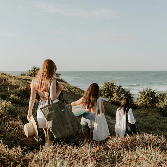 friends walking to beach carrying Sande Kids mesh beach bag on shoulder and surf board.