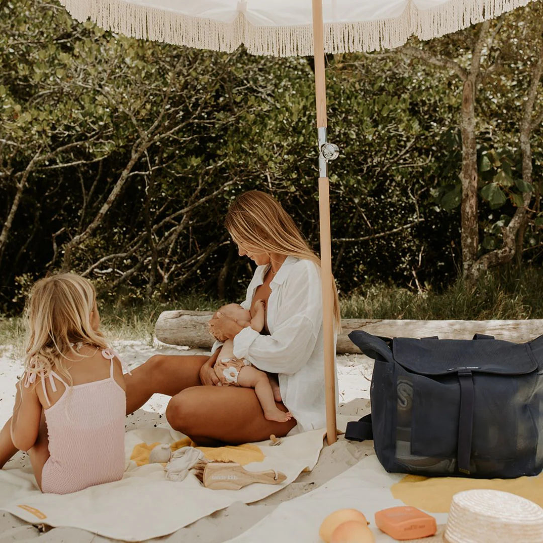 Picnic under umbrella on beach with Sande Kids Beach bag. Mum breastfeeding baby.