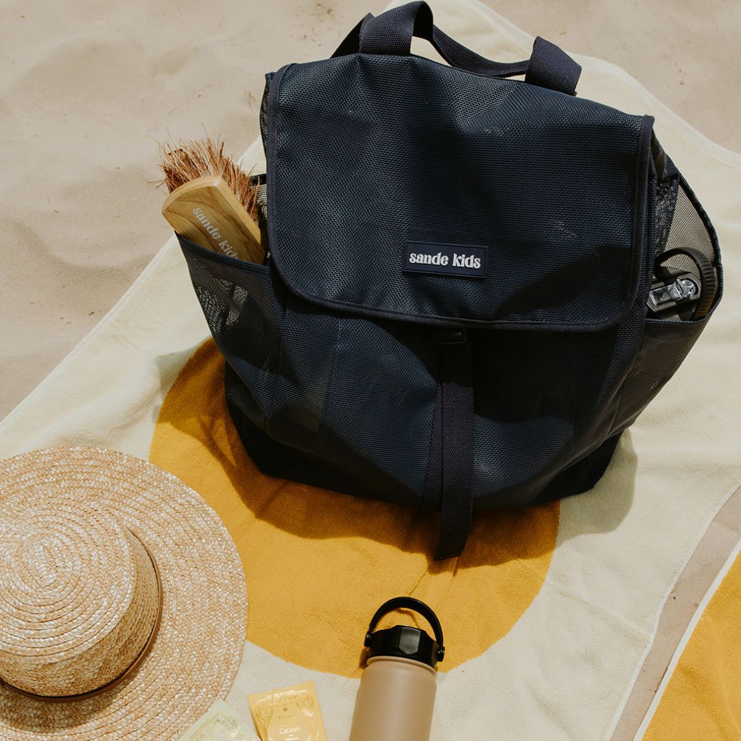 Sande Kids Mesh Beach Backpack on a towel on sand.