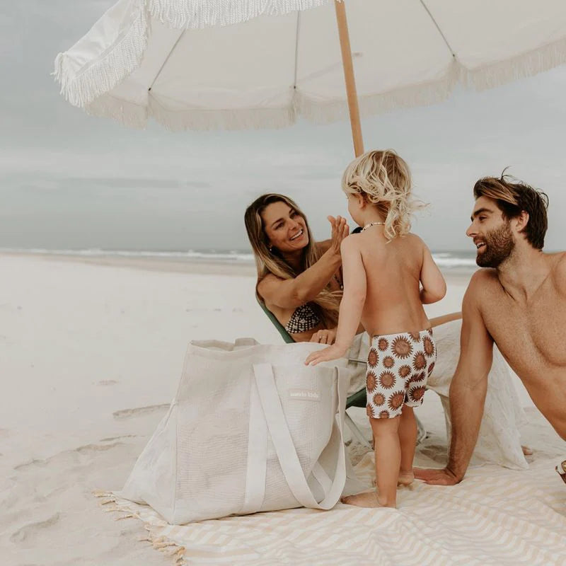 A young family on beach applying sunscreen with the Sande Kids Beach bag.