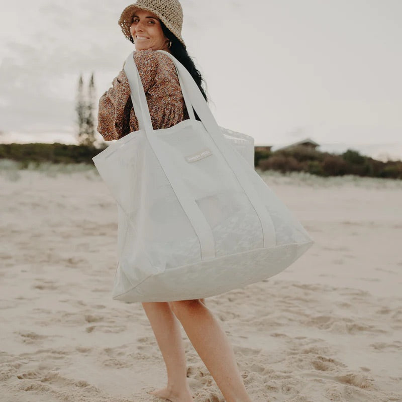 Mum carrying Sand Kids Mesh Beach bag in a neutral colour walking on the sand.