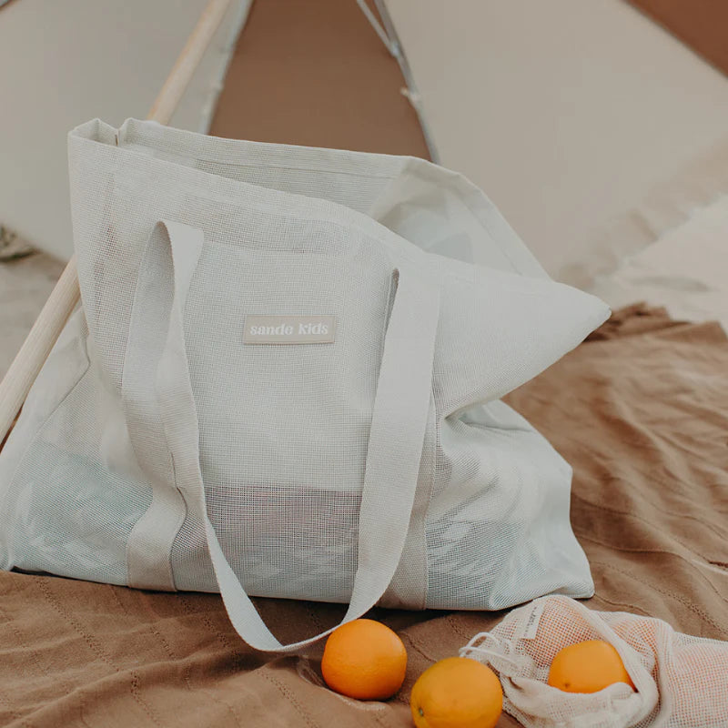 Sande Kids Beach Hauler mesh bag in sand colour sitting on a towel at beach.